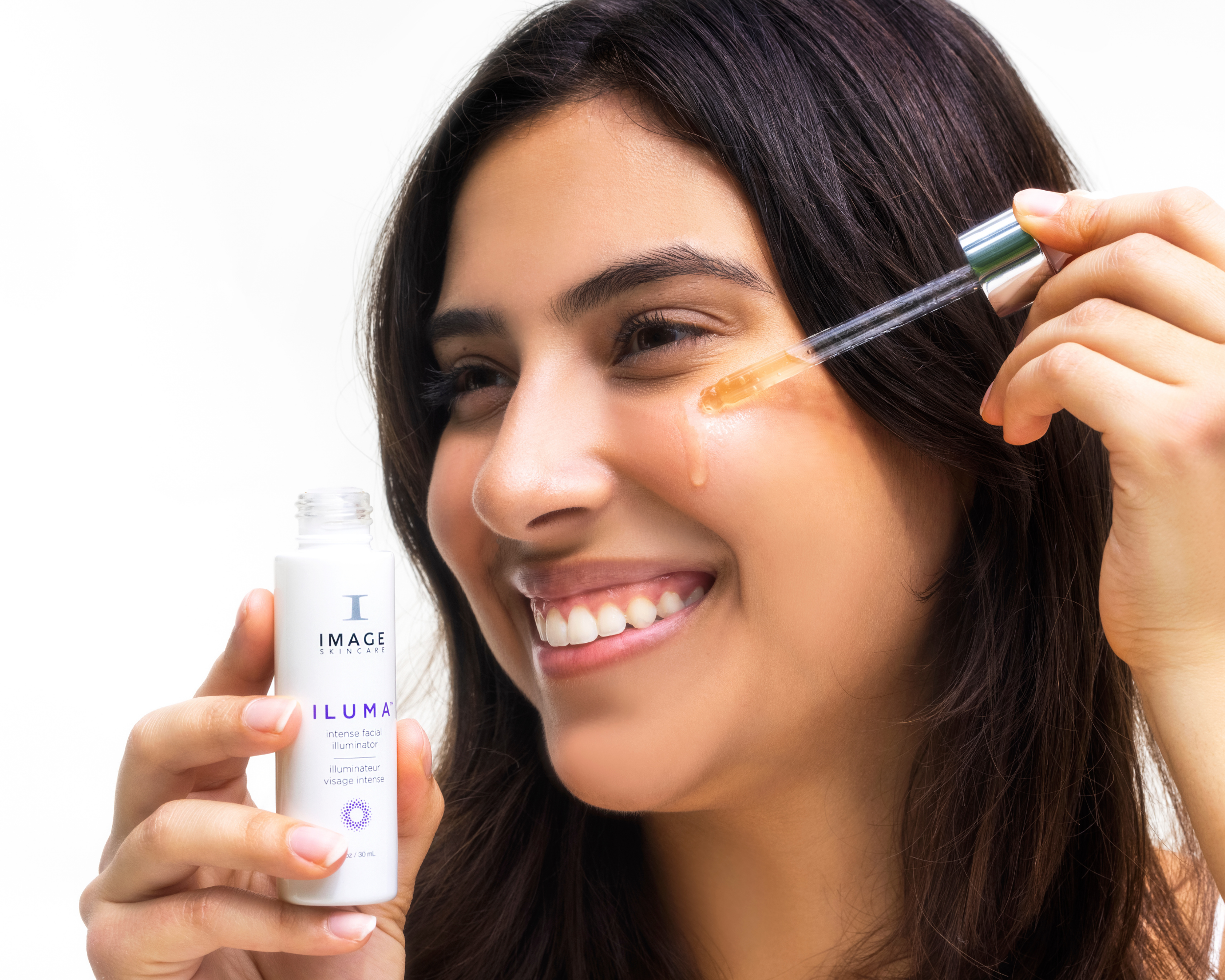 Woman dropping a bottle of IMAGE Skincare Serum onto cheeks