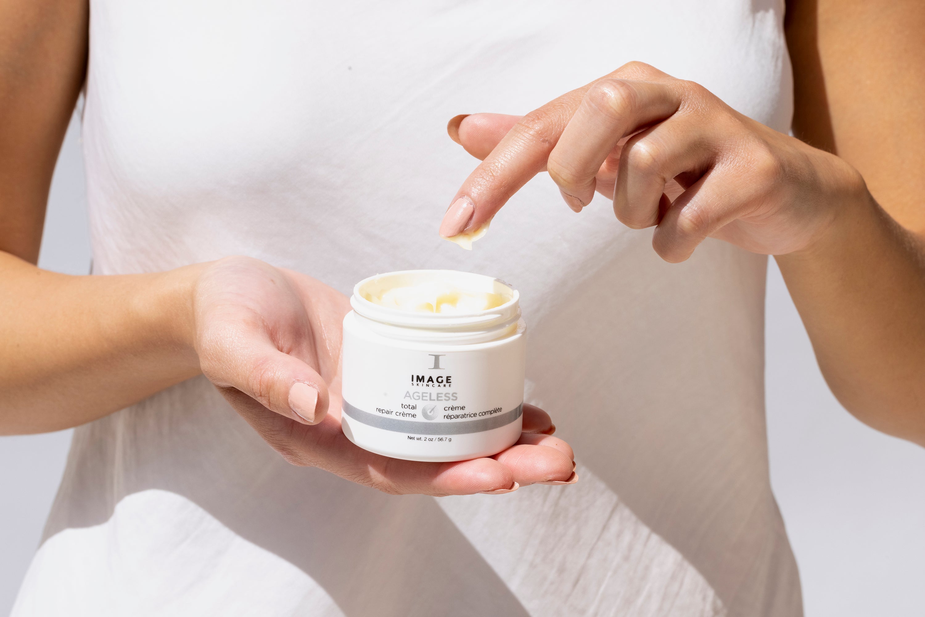 A woman using one finger to apply IMAGE Skincare AGELESS total repair creme.