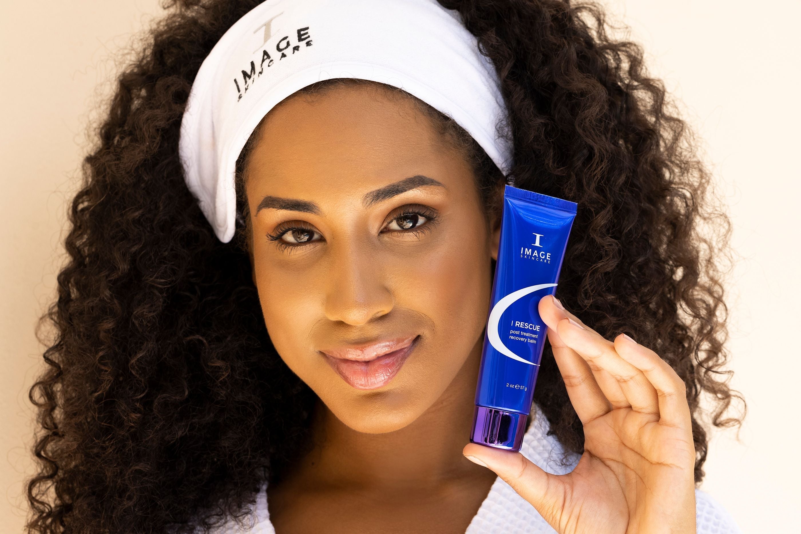 A woman holding up a tube of post treatment recovery balm from IMAGE Skincare.