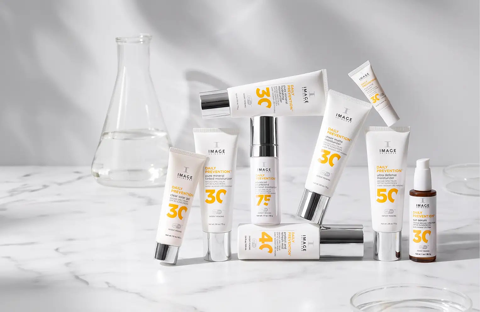 tubes of daily prevention spf products stacked on eachother on light background with a beaker in the back