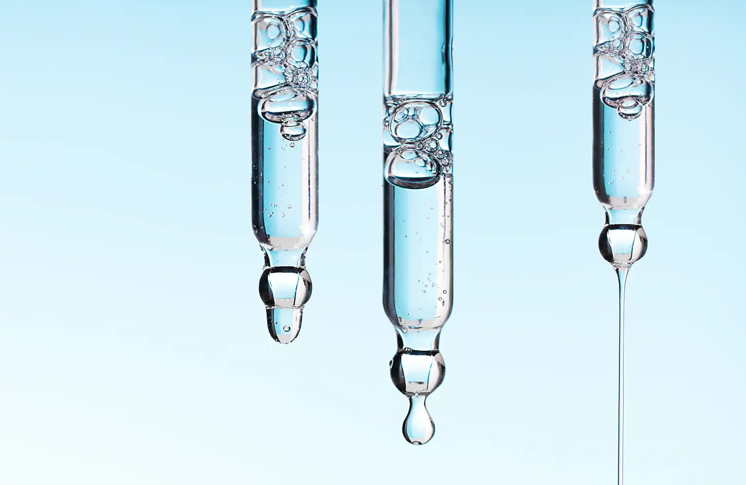 three droppers on light blue background with serum pouring out of them