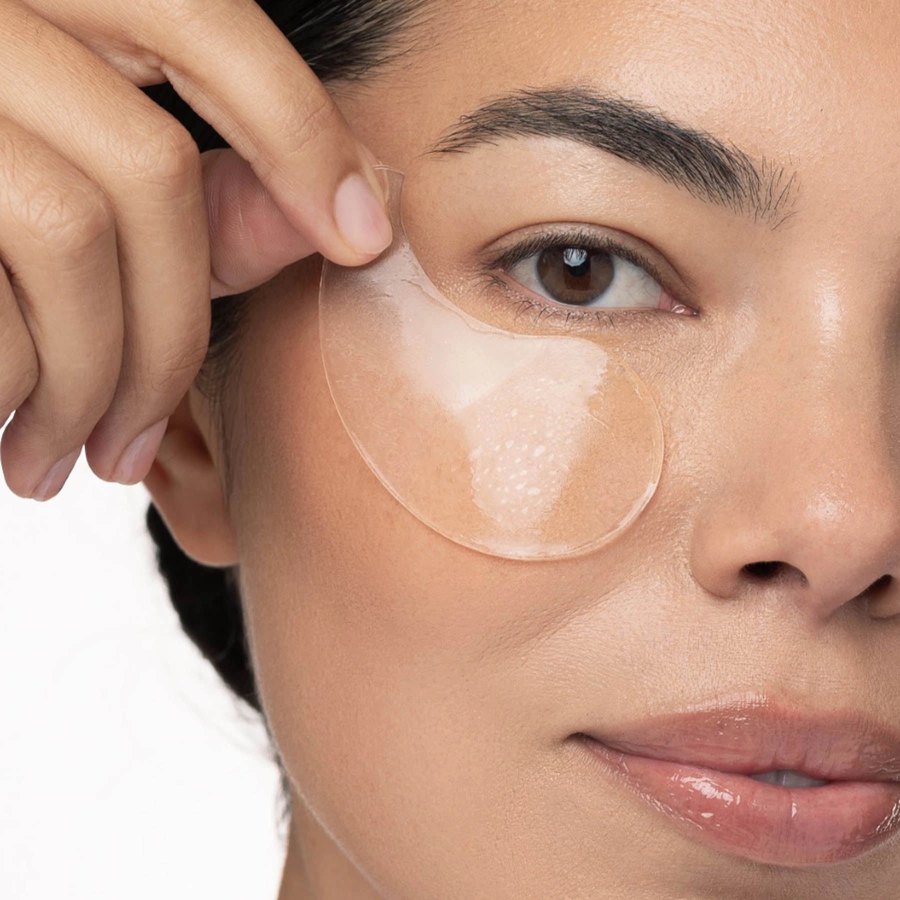 Woman applying a patch under her eye with a neutral background