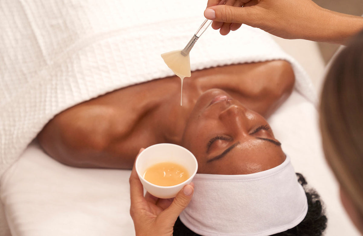model laying down on treatment table with esthetician applying product to face with brush