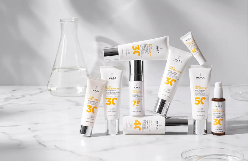 tubes of daily prevention spf products stacked on eachother on light background with a beaker in the back