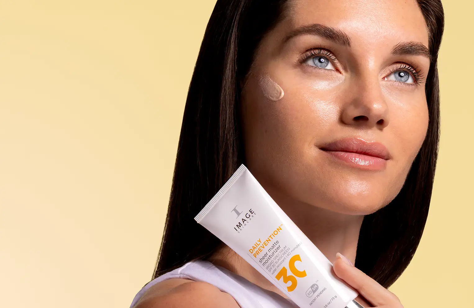 model holding daily prevention spf up to neck with yellow background