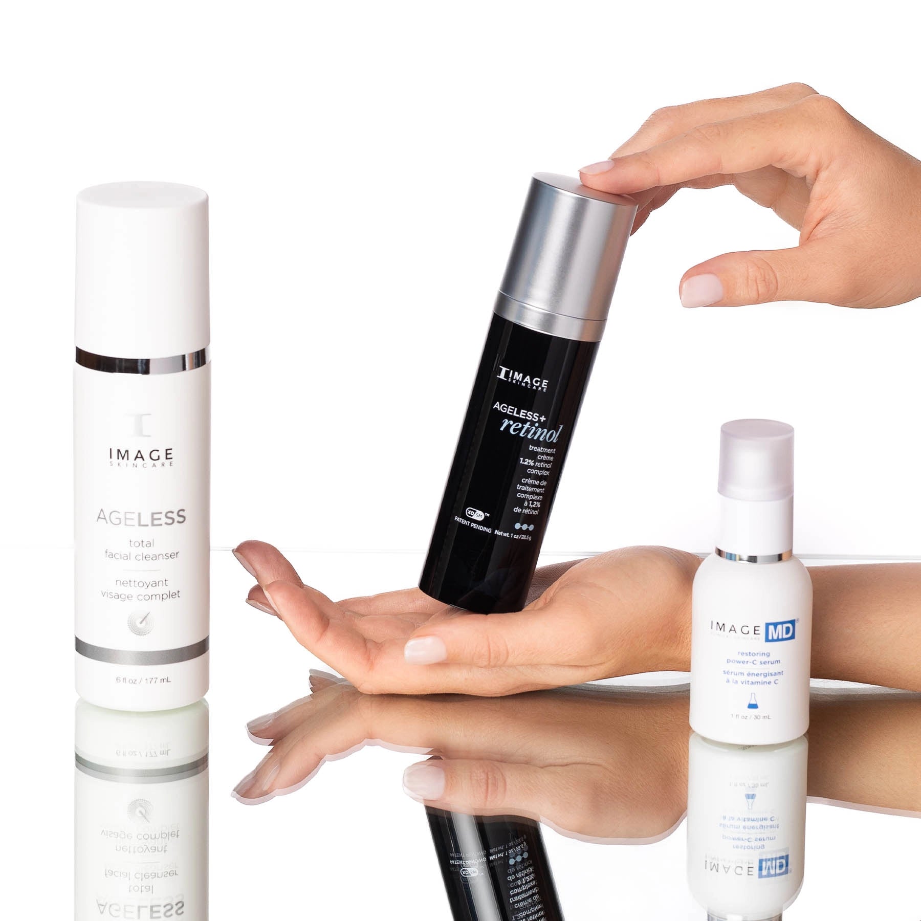 Three skincare products with a hand holding one of them on a reflective surface.