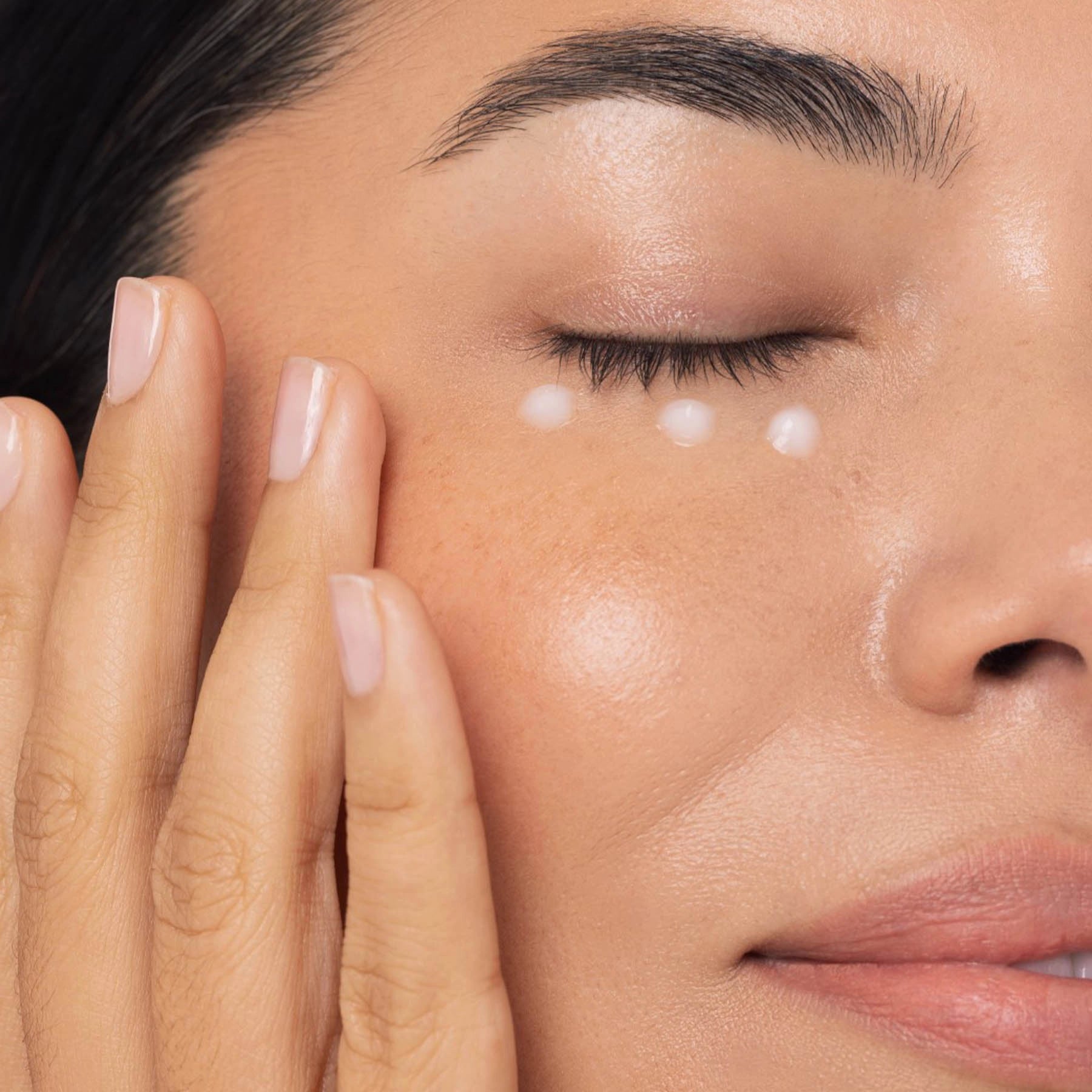 Close-up of a person applying cream to their face with a focus on the skin texture.