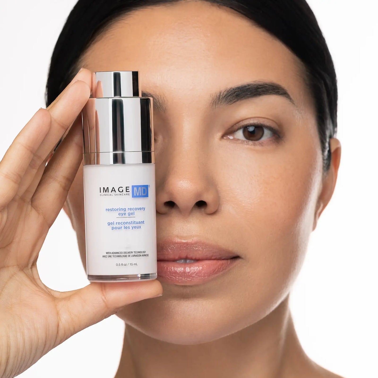 Woman holding a skincare product close to her face on a white background