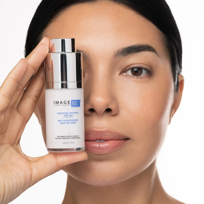 Woman holding a skincare product close to her face on a white background
