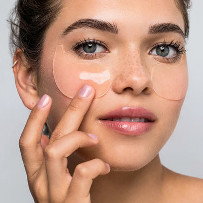 Woman applying eye masks under her eyes with a neutral background