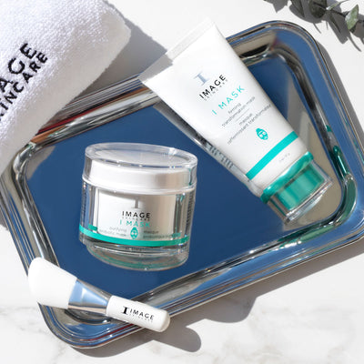 Skincare products including a jar and tube labeled 'IMAGE' on a reflective surface.