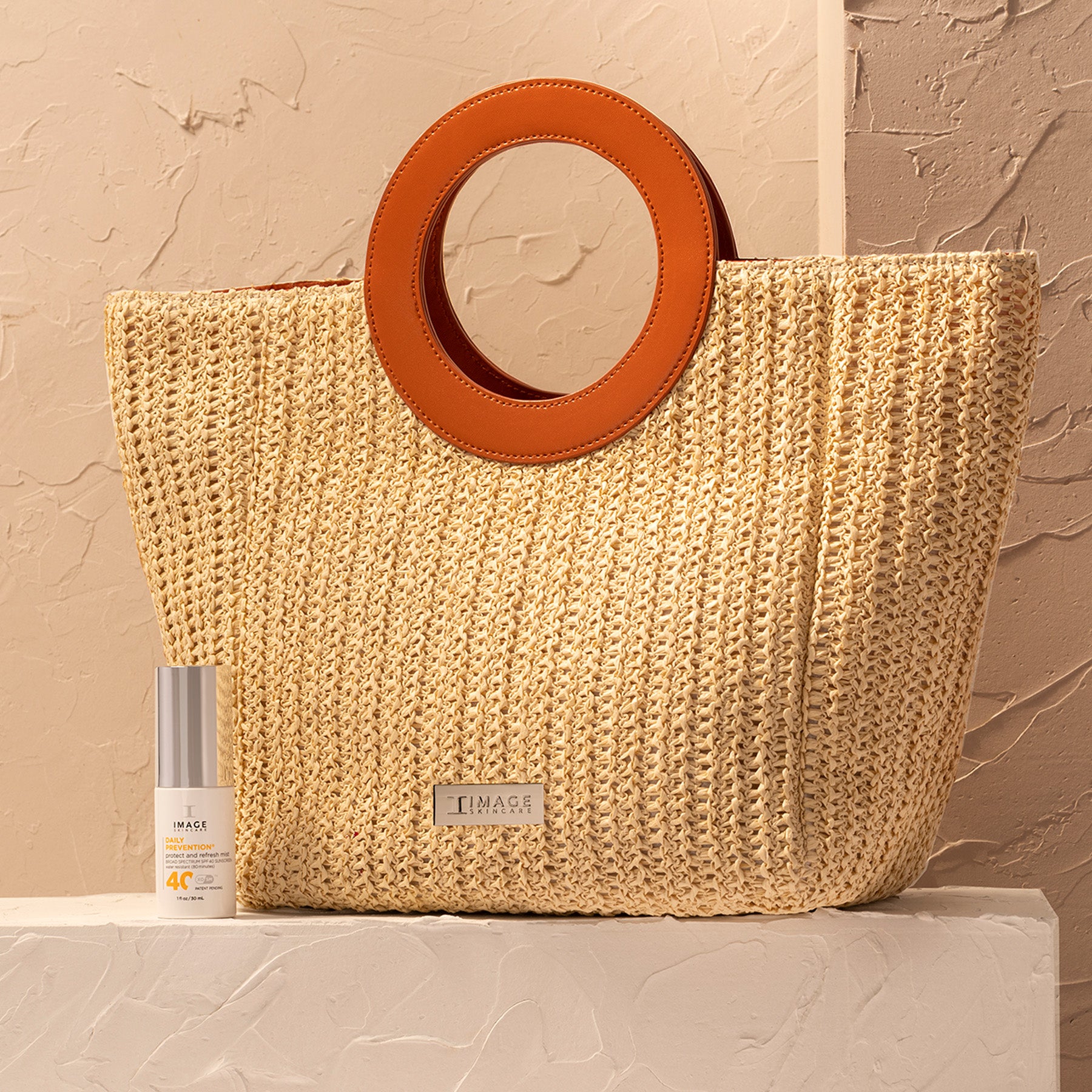 Woven beige bag with brown circular handle on a textured surface