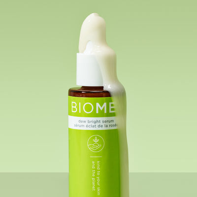 bottle of dew bright serum with product pouring down the side of bottle on a green background