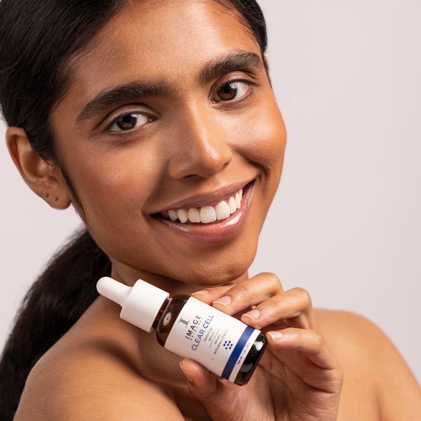 model smiling and holding clear cell restoring serum bottle