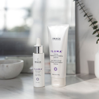 iluma intense facial illuminator bottle and exfoliating cleanser tube on bathroom counter