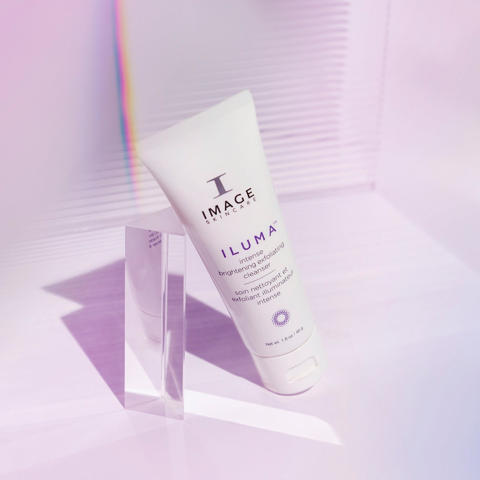 iluma cleanser travel size tube leaning against a prism on a light purple background