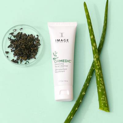 travel size ormedic cleanser laying in between petri dish with ingredient and aloe plant leaves