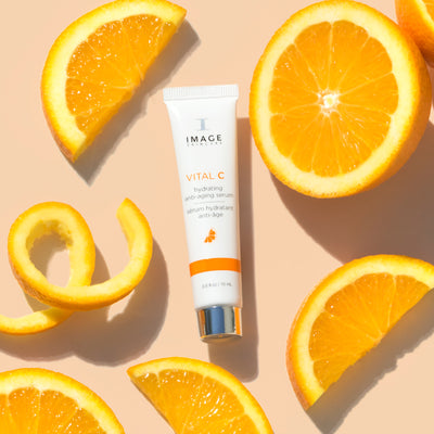 travel size anti-aging serum on orange background with orange slices