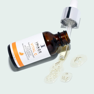 bottle of ACE serum open with dropper dripping oil on light background