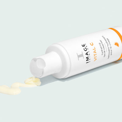 bottle of cleanser open with cleanser pouring out on light background