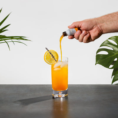 model hand pouring liquid collagen into bright orange drink 